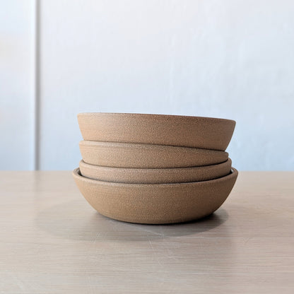Stack of brown ceramic bowls on a light wooden surface with a light blue wall background