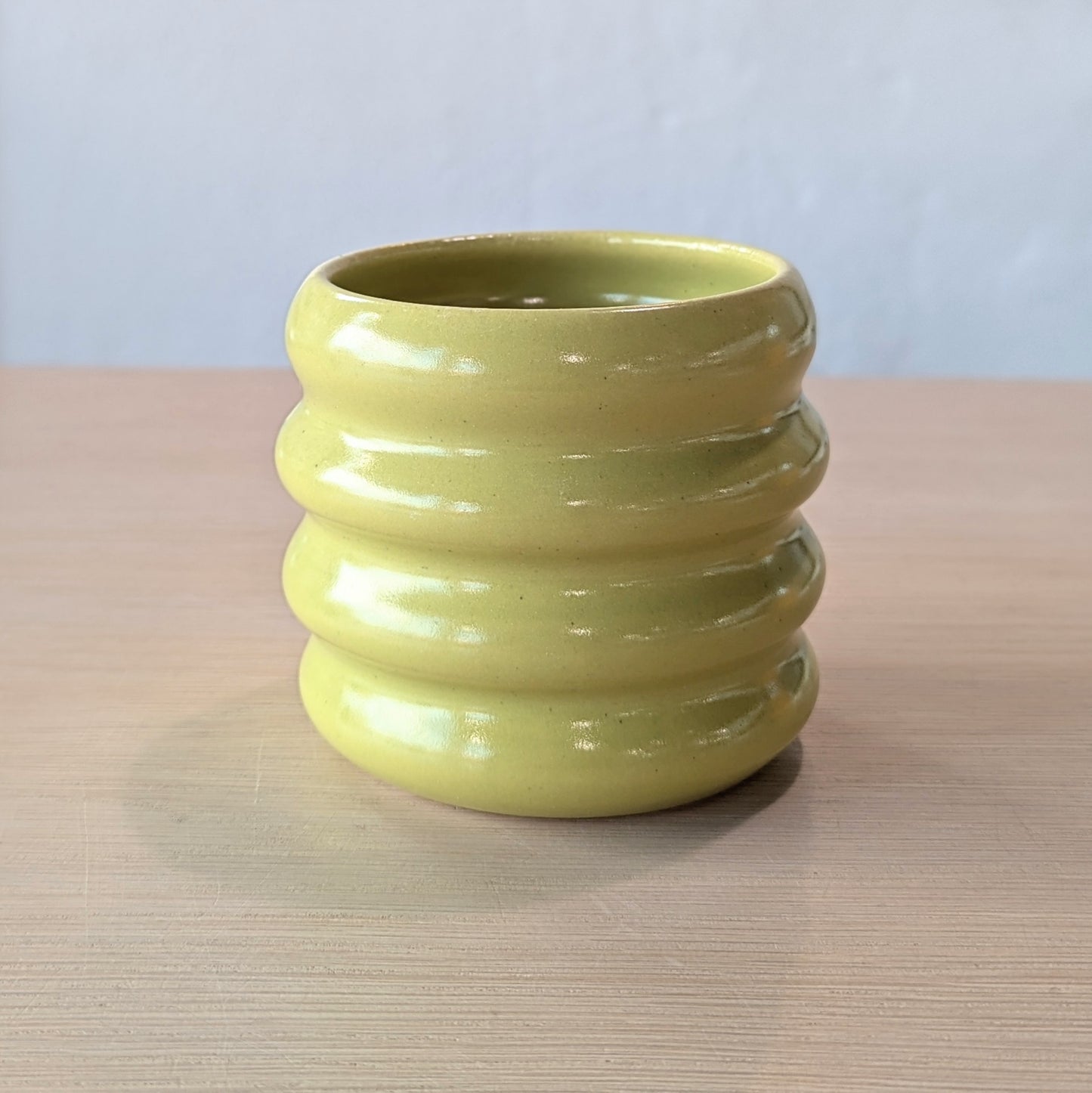 lime green ceramic tumbler on a wooden surface with a white wall background.