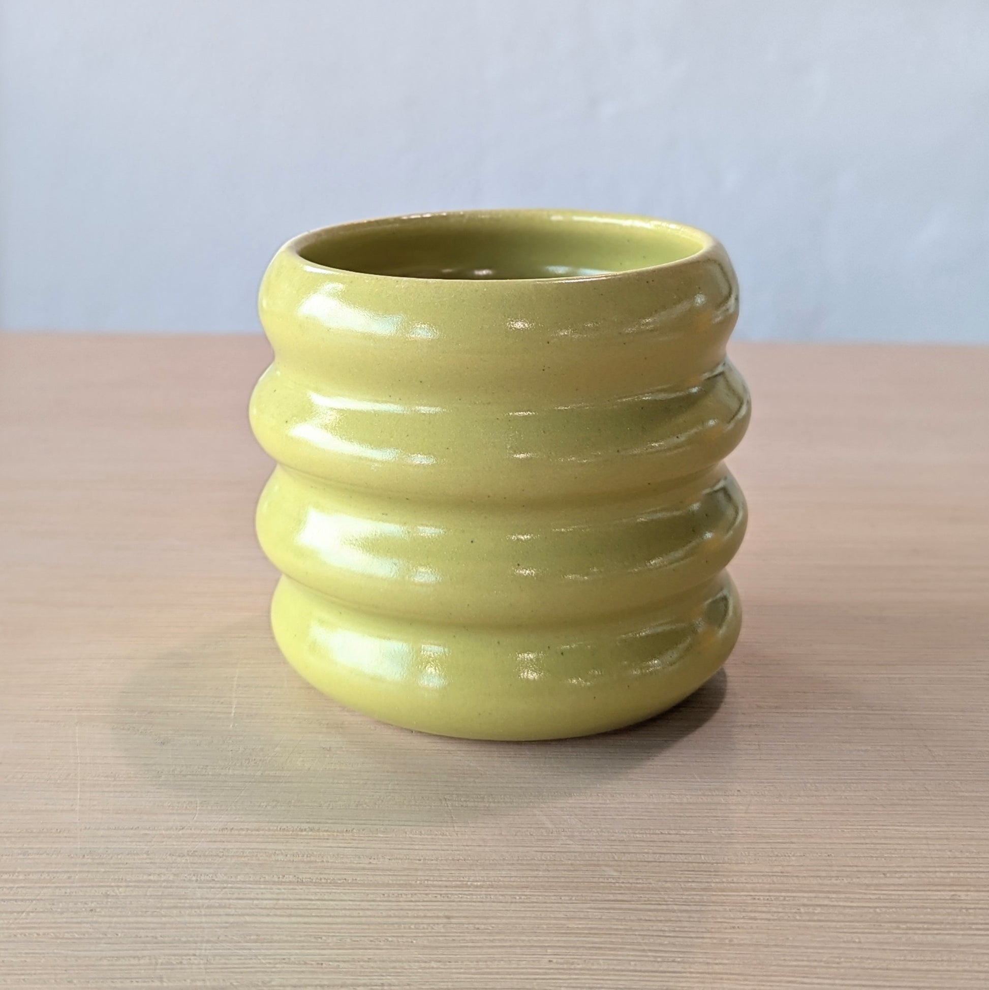 lime green ceramic tumbler on a wooden surface with a white wall background.