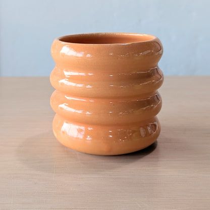 orange ceramic tumbler on a wooden surface with a white wall background.